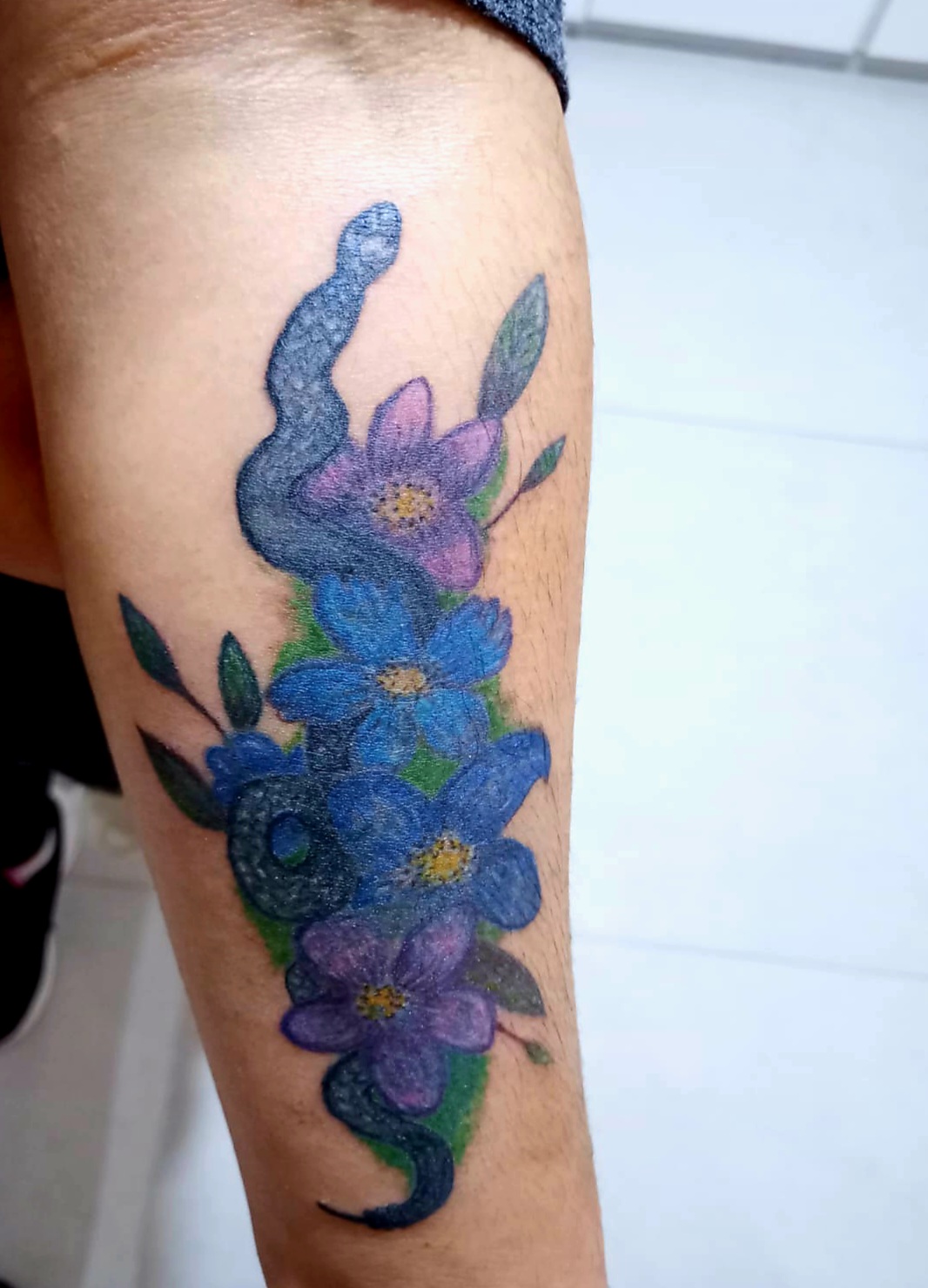 Detalle de tatuaje botánico en el antebrazo con flores y helechos en técnica fine-line de alta precisión